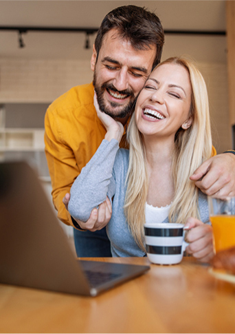 Couple smiling at each other at their laptop.